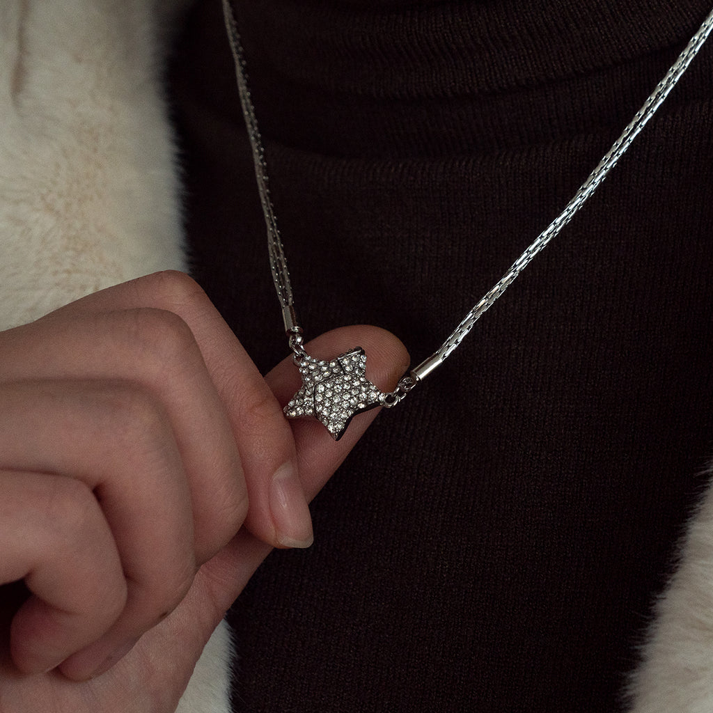 Star-shaped pendant necklace held by a hand against a dark background