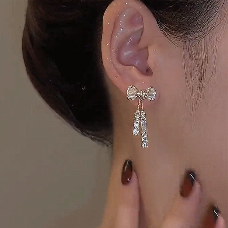 Close-up of an ear wearing a bow-shaped earring with dangling crystals.