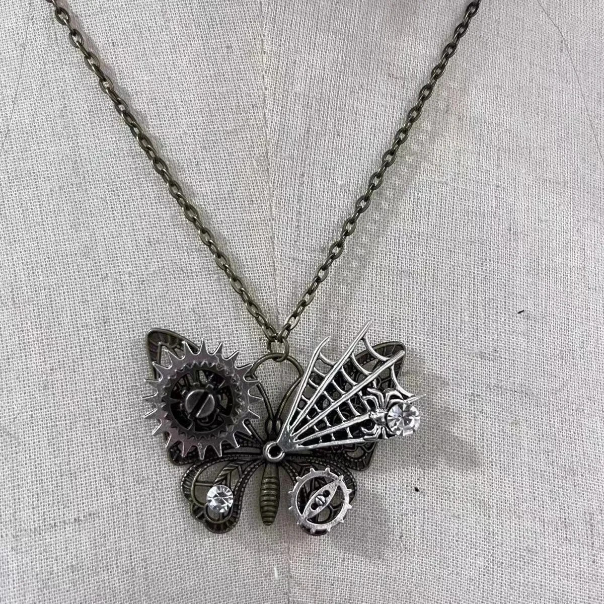 Steampunk-style butterfly necklace with gears and crystals on a light fabric background