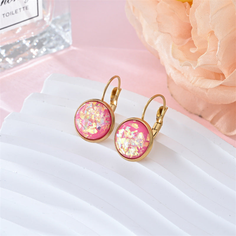 Pink glittery earrings with gold hooks on a white surface with a pink flower in the background.