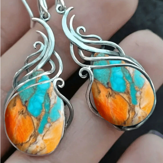 Turquoise and orange stone earrings with silver wire wrapping held in hand