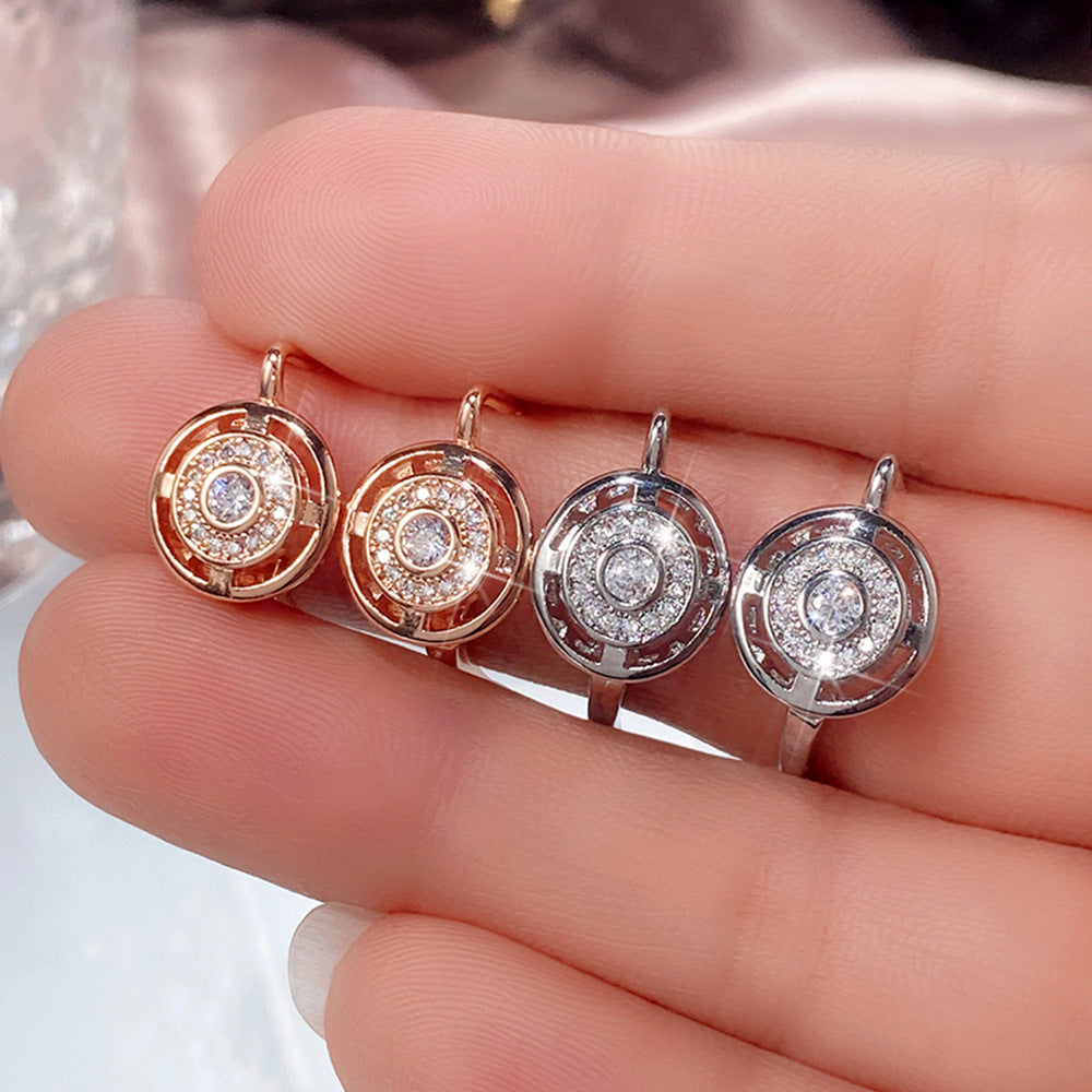 Four circular earrings with diamond-like stones held between fingers.