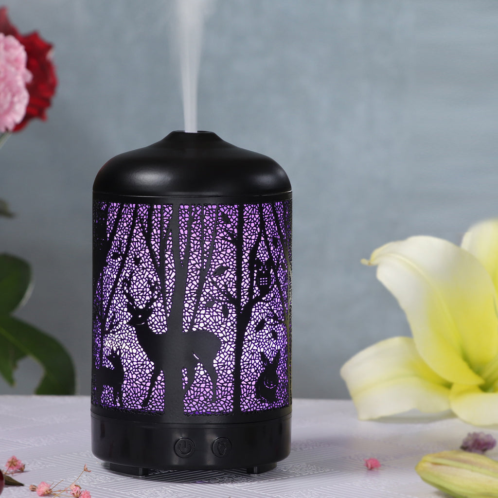 Black essential oil diffuser with purple tree design on a gray background with flowers.