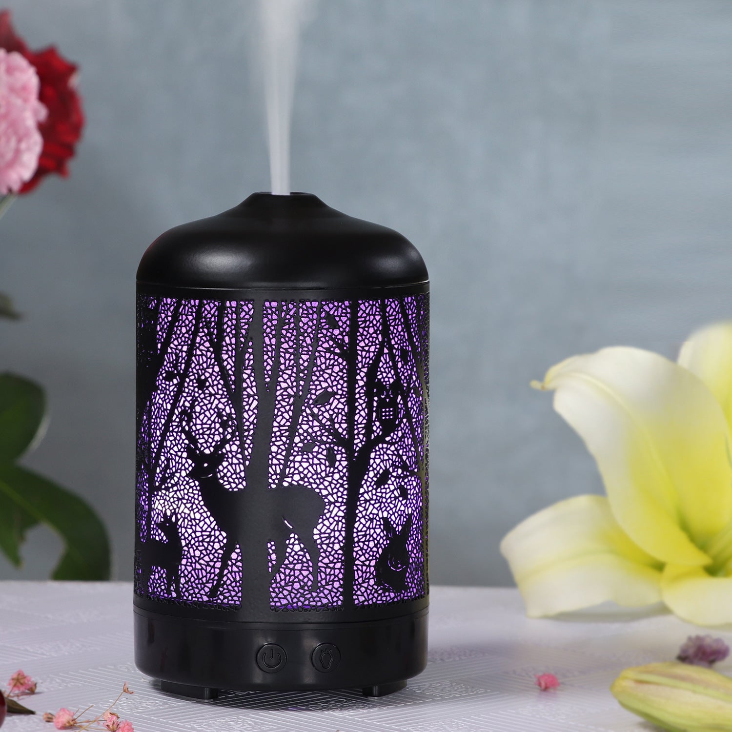 Black essential oil diffuser with purple tree design on a gray background with flowers.
