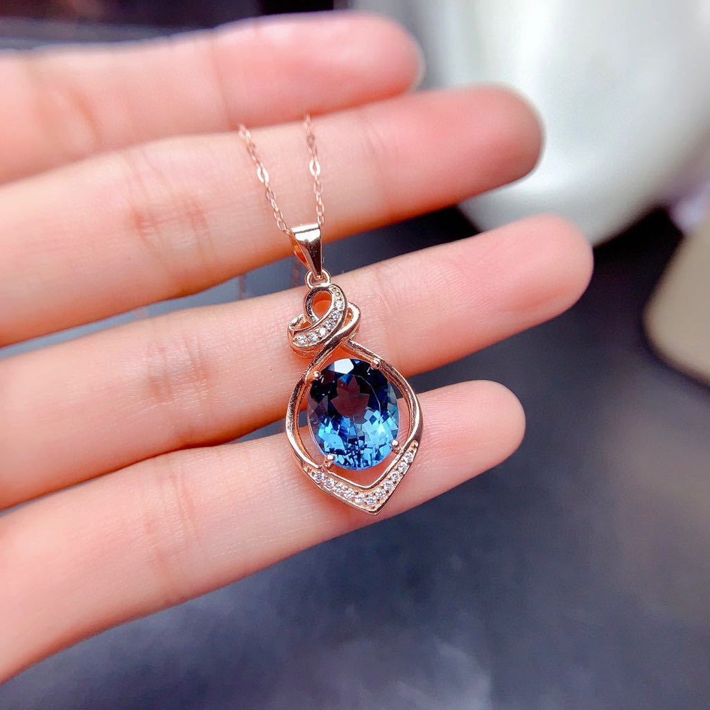 Rose gold necklace with a blue gemstone pendant held in a hand.