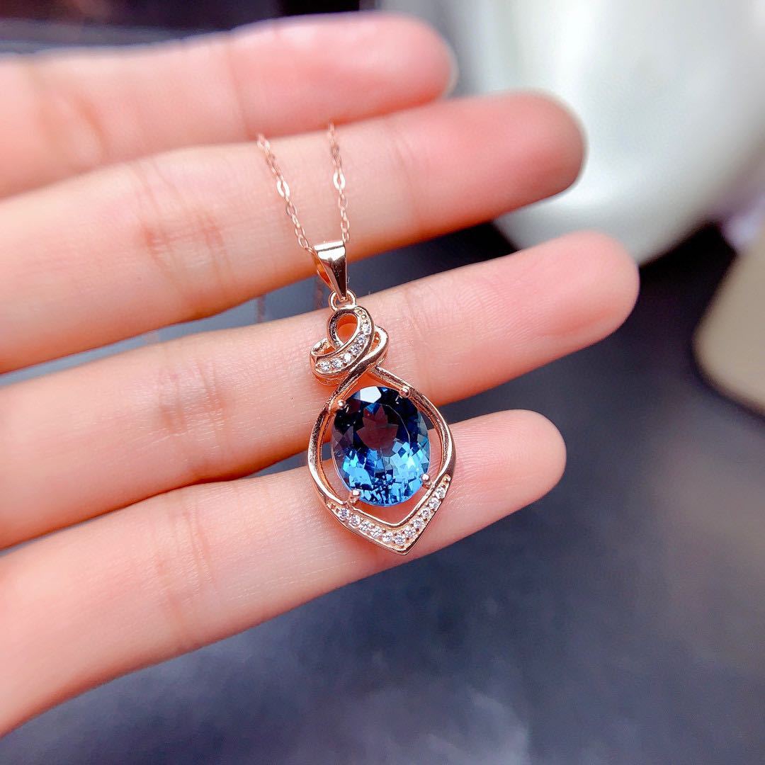 Rose gold necklace with a blue gemstone pendant held in a hand.