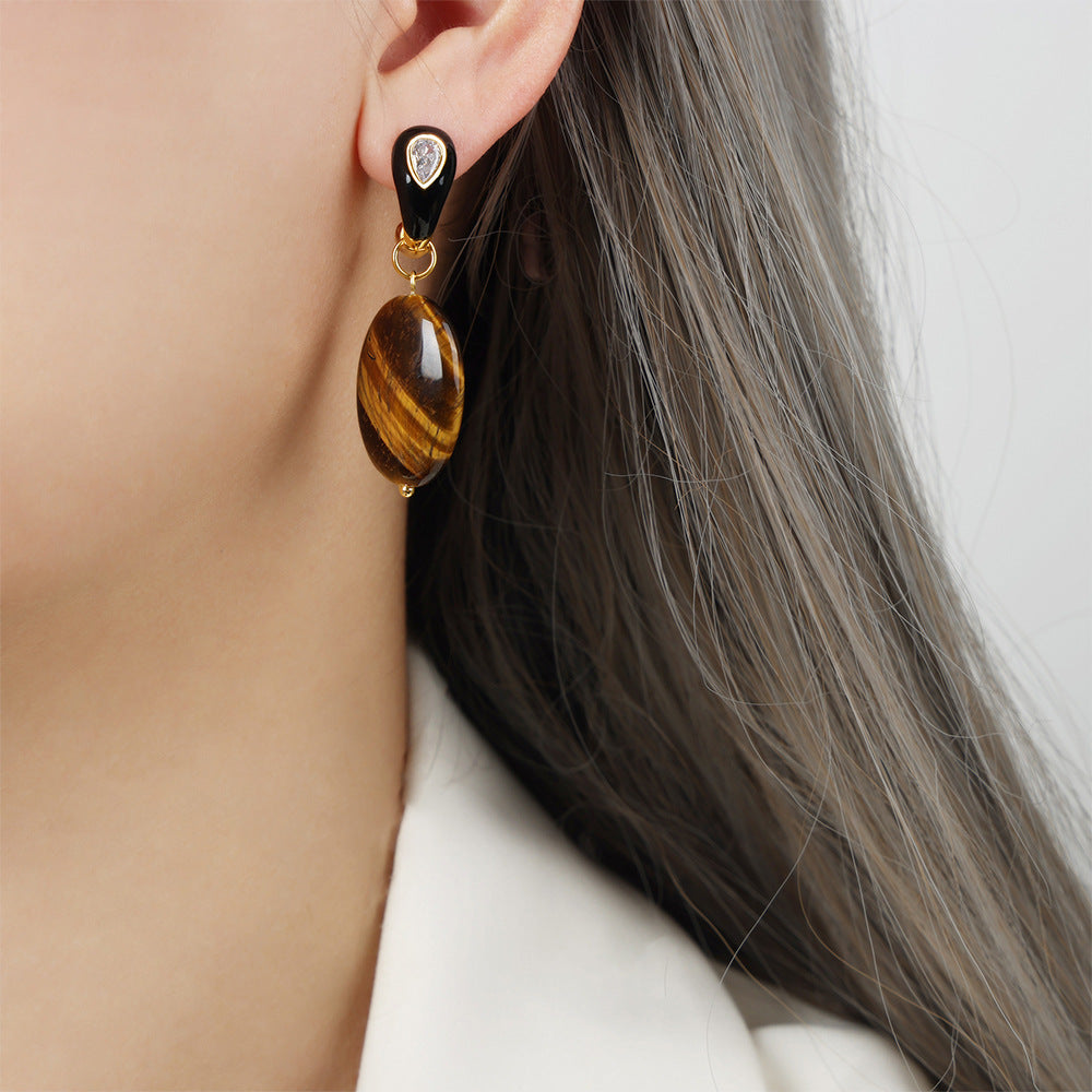 Close-up of a person wearing a gold earring with a tiger's eye stone.