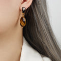 Close-up of a person wearing a gold earring with a tiger's eye stone.