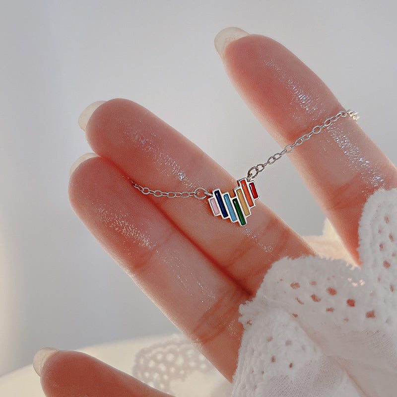 Silver necklace with colorful pendant held by a hand against a light background