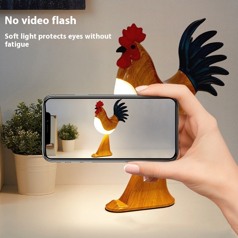 Rooster-shaped lamp with soft light being captured on a smartphone screen.