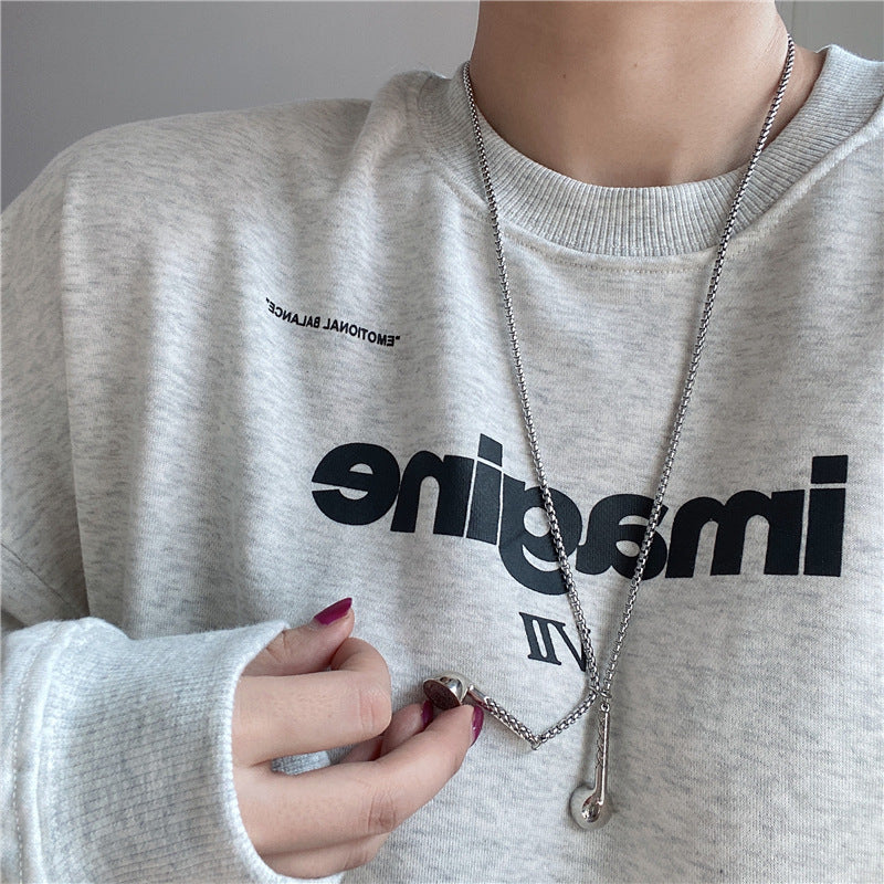 Person wearing a gray sweatshirt with black text and holding a silver necklace.