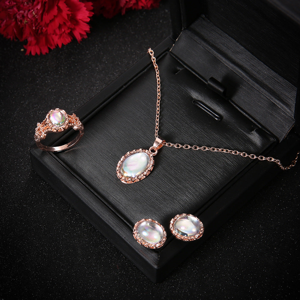 Rose gold jewelry set with necklace, earrings, and ring on a black stand with red flowers in the background.