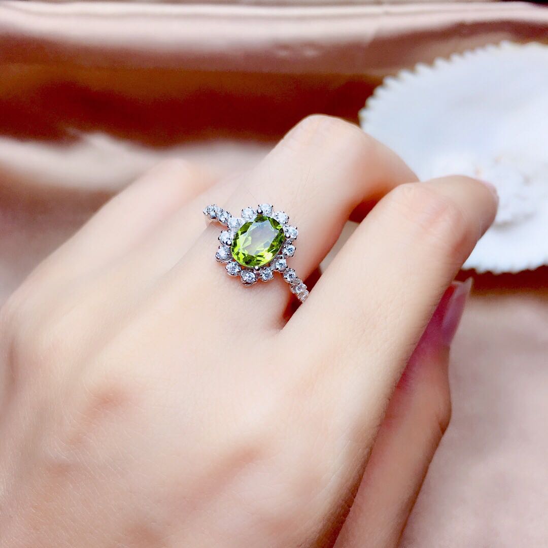 Hand wearing a ring with a green gemstone on a soft pink fabric background