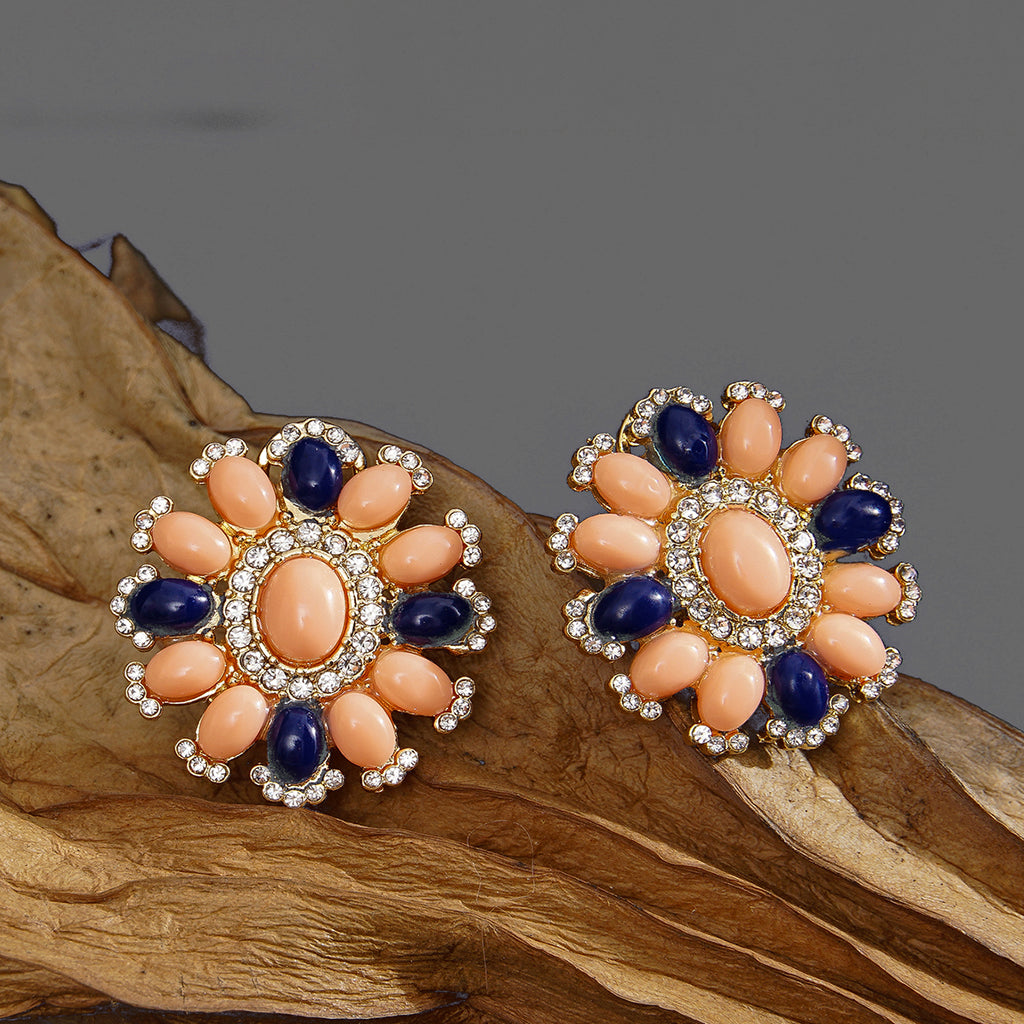 Pair of floral earrings with peach and blue stones on a wooden surface