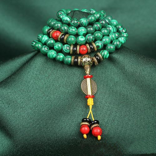 Green beaded bracelet with red and gold accents on a green fabric background