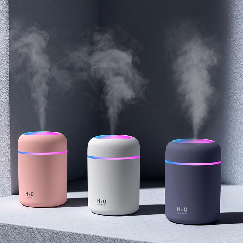 Three humidifiers in pink, white, and black emitting steam on a dark background.