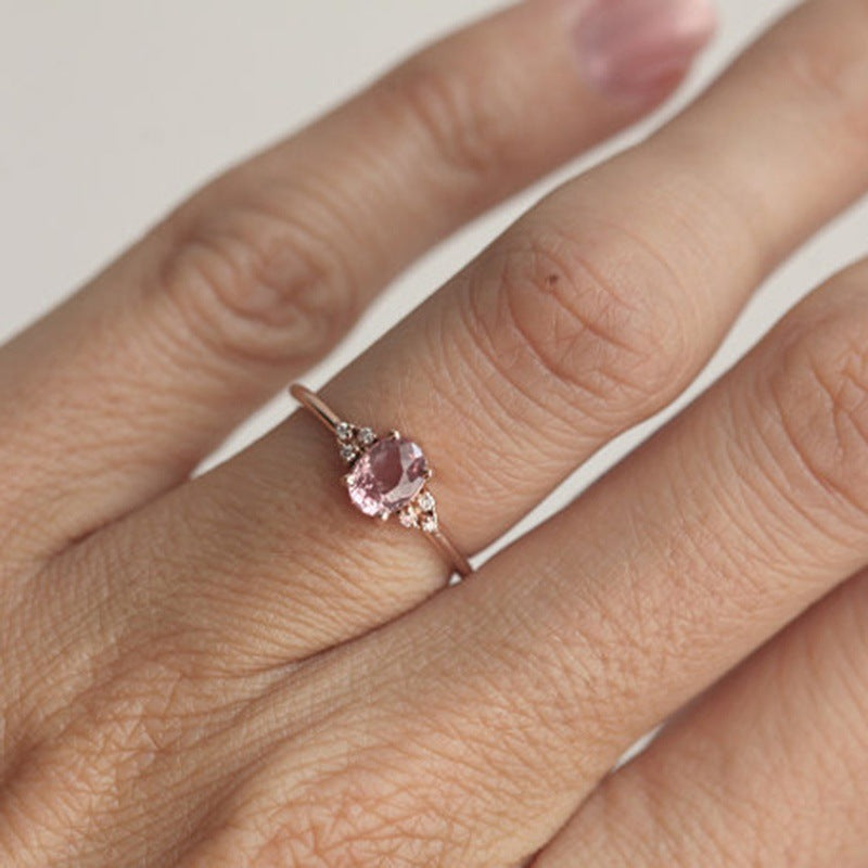 Rose gold ring with a pink gemstone on a finger against a neutral background