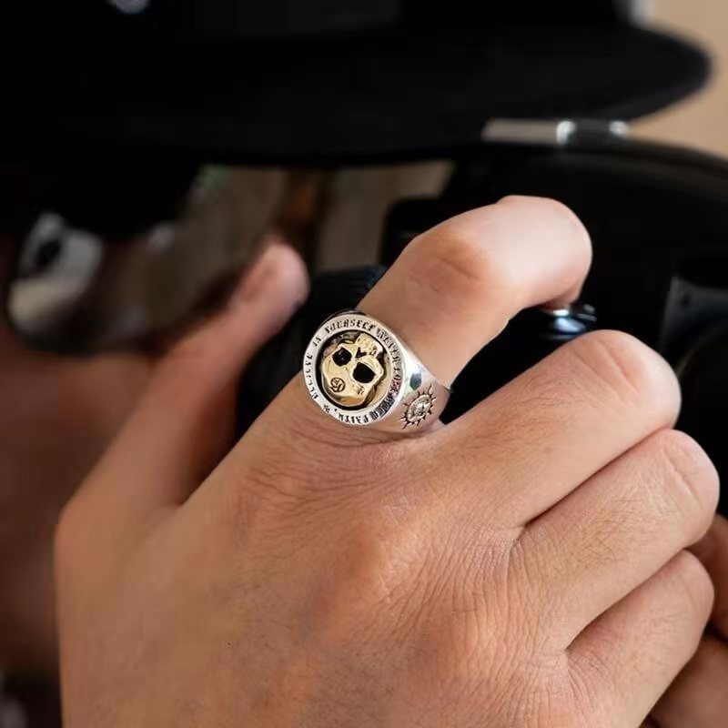 Hand wearing a silver ring with a black and gold design, holding a black object.