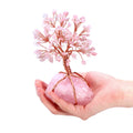 Pink wire tree on a pink stone held in a hand against a white background