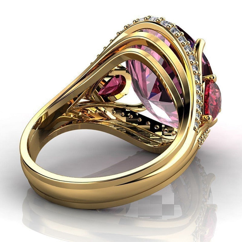 Gold ring with pink gemstone and red accents on a white background