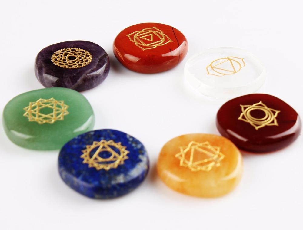 Set of seven chakra stones with colorful surfaces and gold symbols on a white background