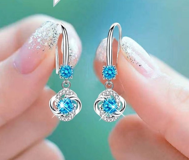Silver earrings with blue gemstones held between fingers against a blurred background
