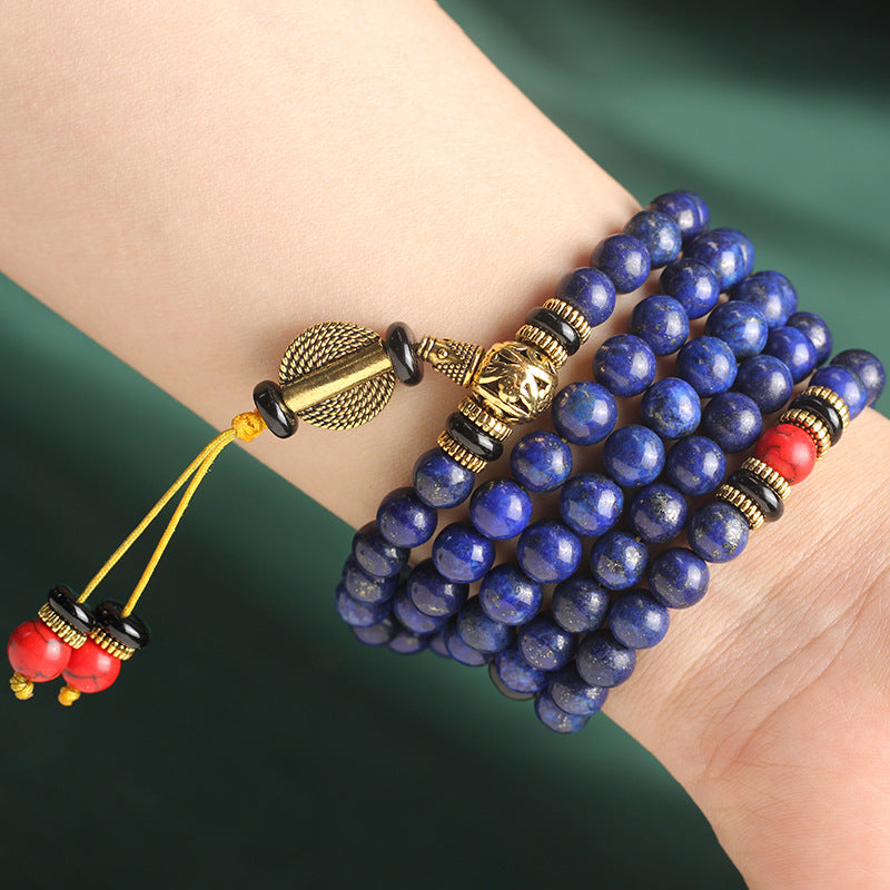 Blue beaded bracelet with gold and red accents on a wrist against a green background