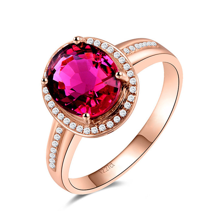 Rose gold ring with a large red gemstone and smaller diamonds on a white background