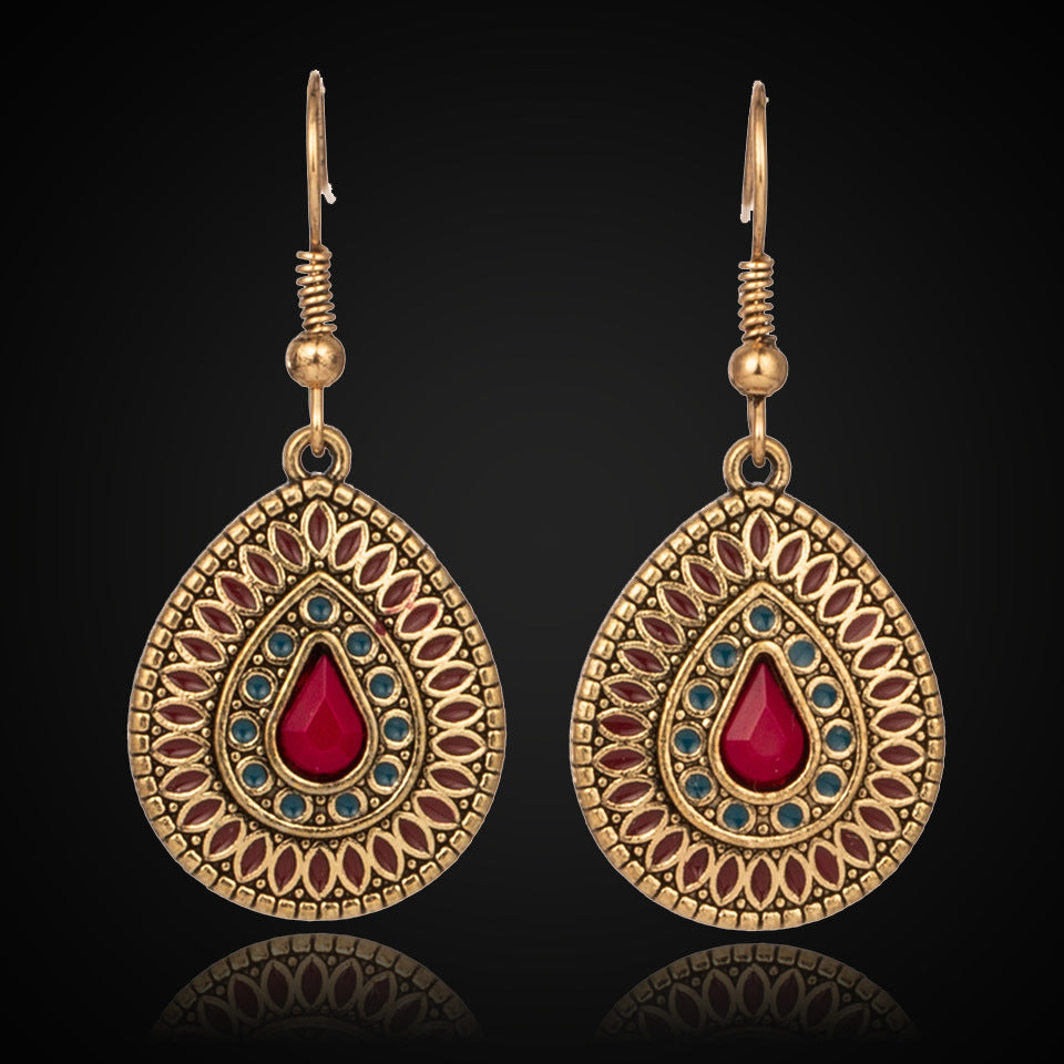 Pair of ornate earrings with red and blue stones on a black background