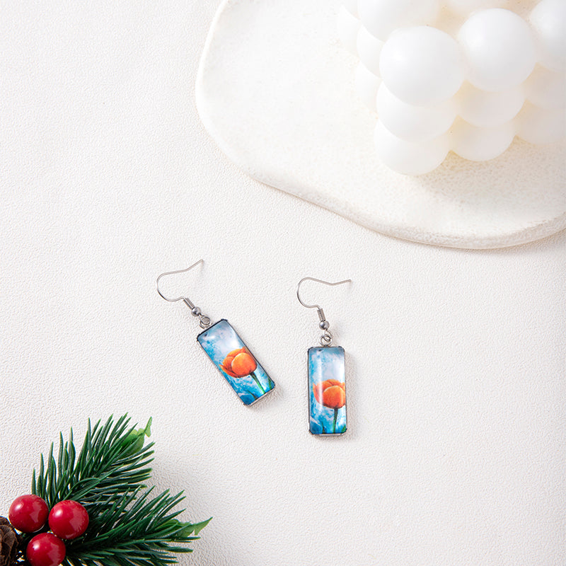 Pair of earrings with a scenic design on a white surface with decorative elements.