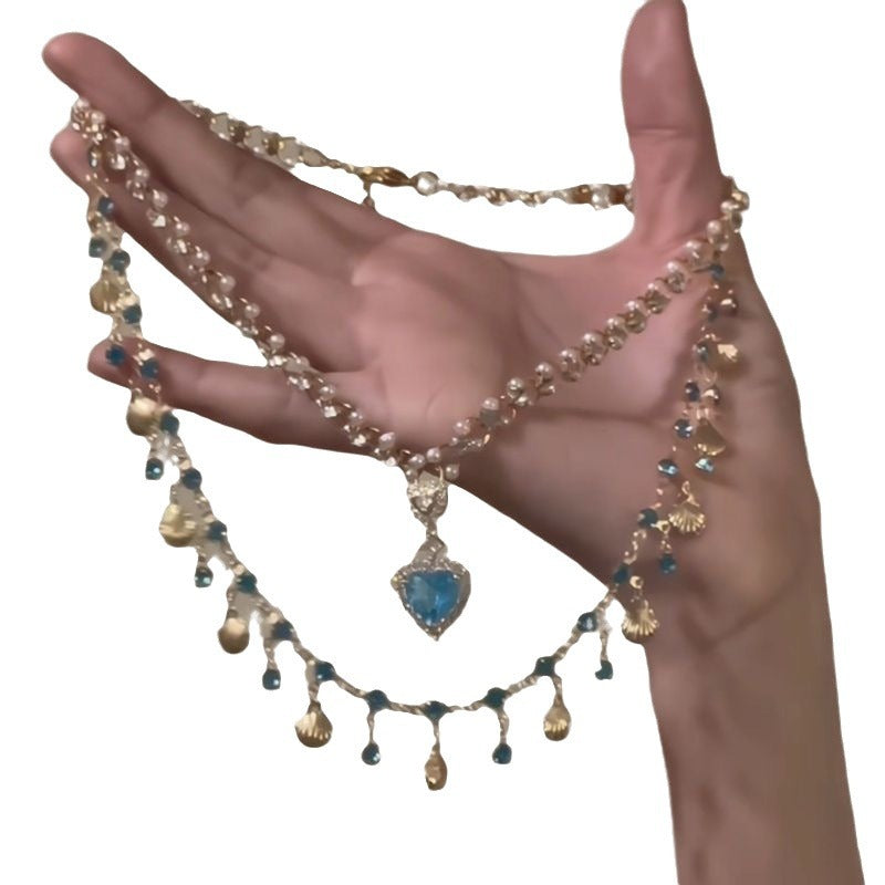 Hand holding a decorative necklace with beads and a blue pendant on a white background