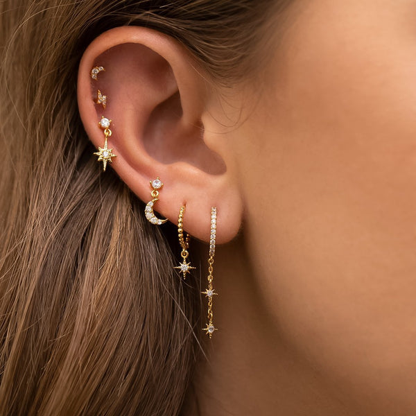 Close-up of an ear with gold earrings featuring stars and moons.