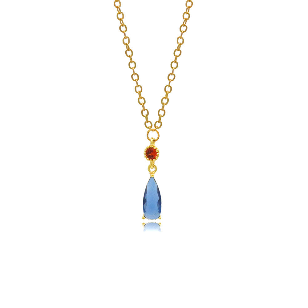 Gold necklace with a blue teardrop pendant and red gemstone on a white background