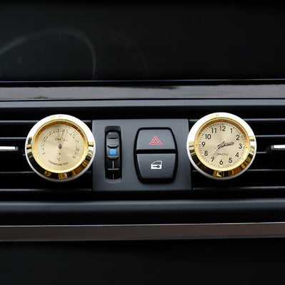 Gold car air freshener with clock design on a car vent.