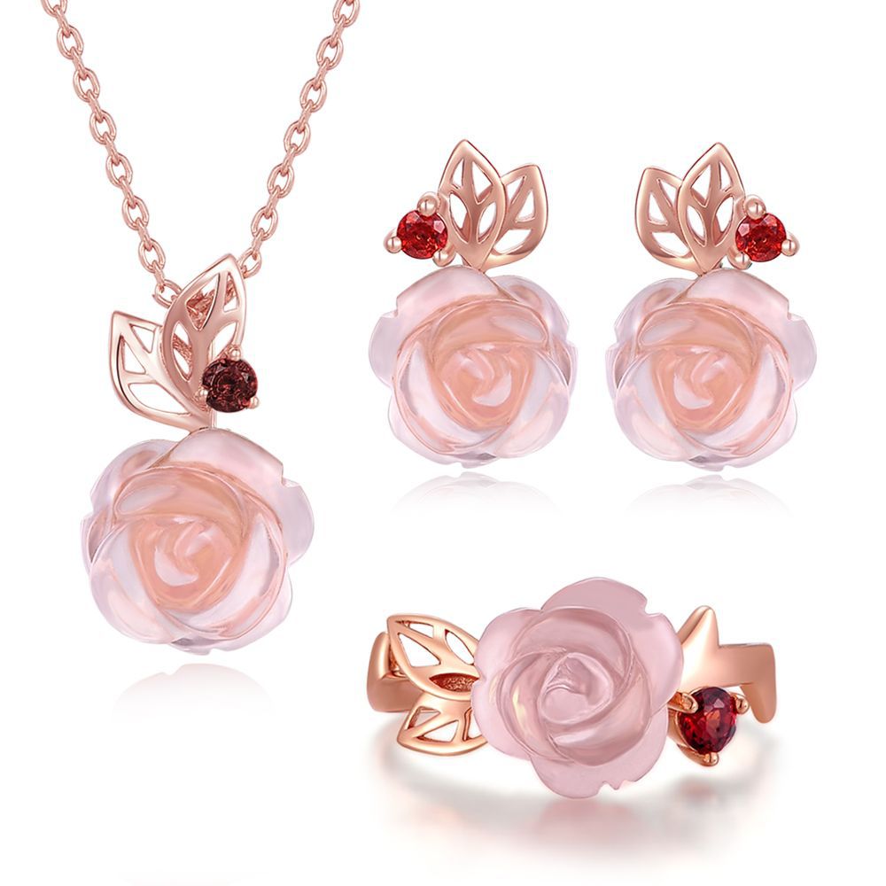 Rose gold jewelry set with pink rose flowers and red gemstones on a white background