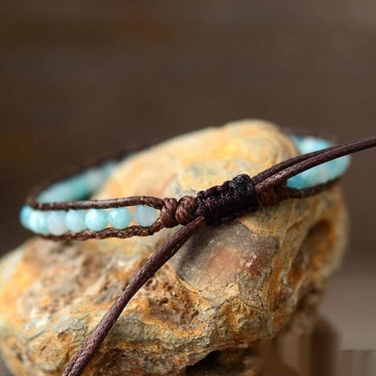 Bracelet with turquoise beads and brown cord on a rock, Free Spirit Shop branding visible