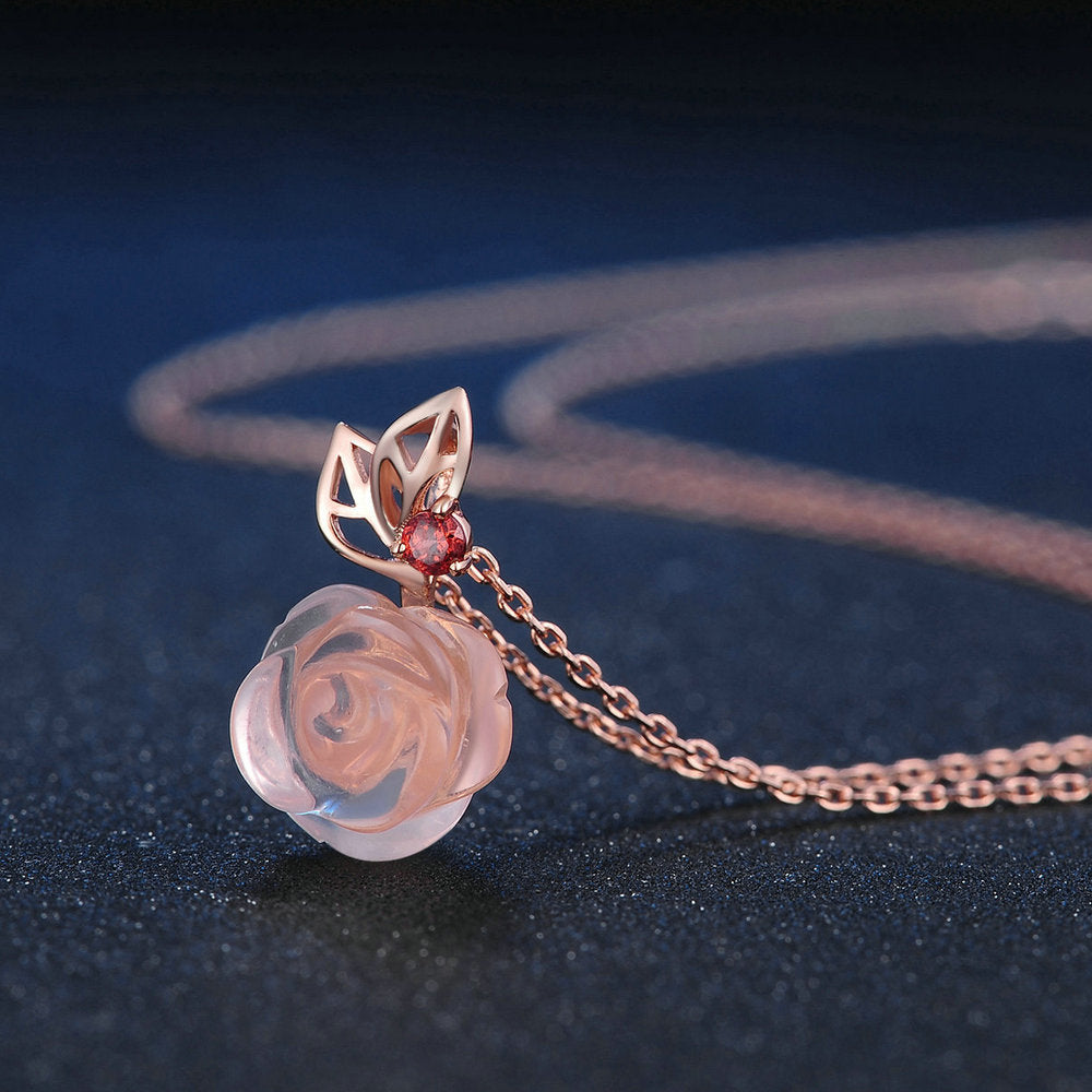 Rose gold necklace with a rose pendant and red gemstone on a dark background