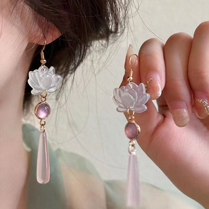 Lotus flower earrings with pink teardrop charms worn by a person.