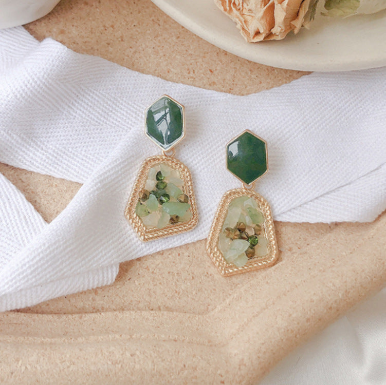 Pair of gold and green earrings on a white fabric background