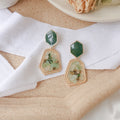 Pair of gold and green earrings on a white fabric background