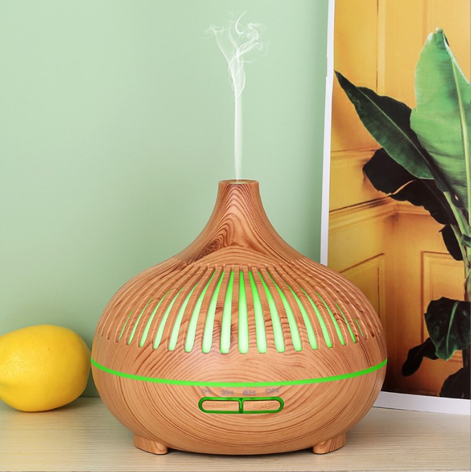 Wooden diffuser with green accents on a surface with a light green wall and plant in the background