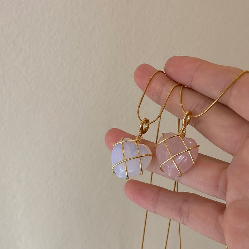 Hand holding gold earrings with pink and blue gemstones against a beige background