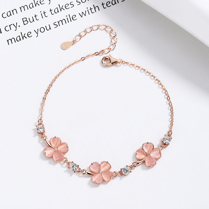 Rose gold bracelet with pink floral charms on a white background