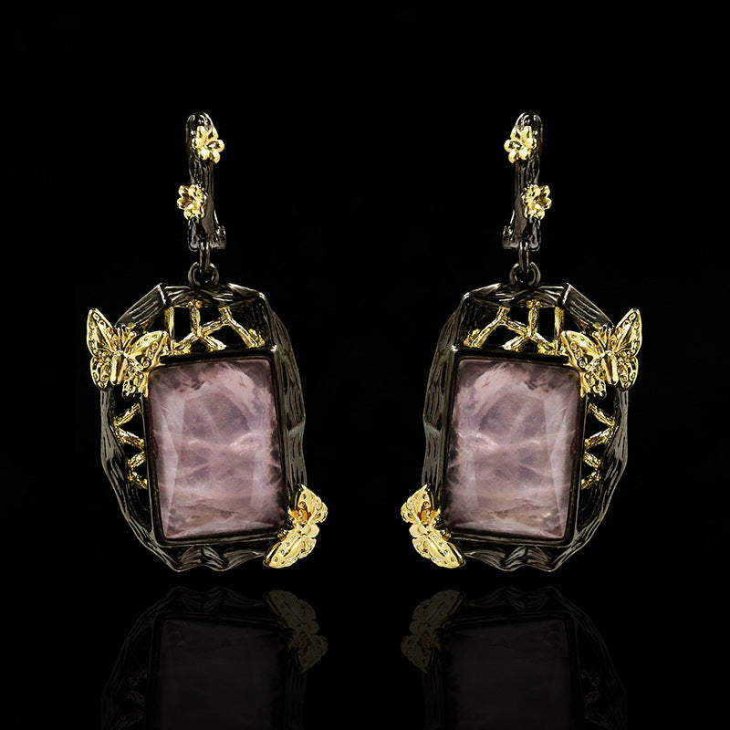 Pair of earrings with purple stones and gold accents on a black background