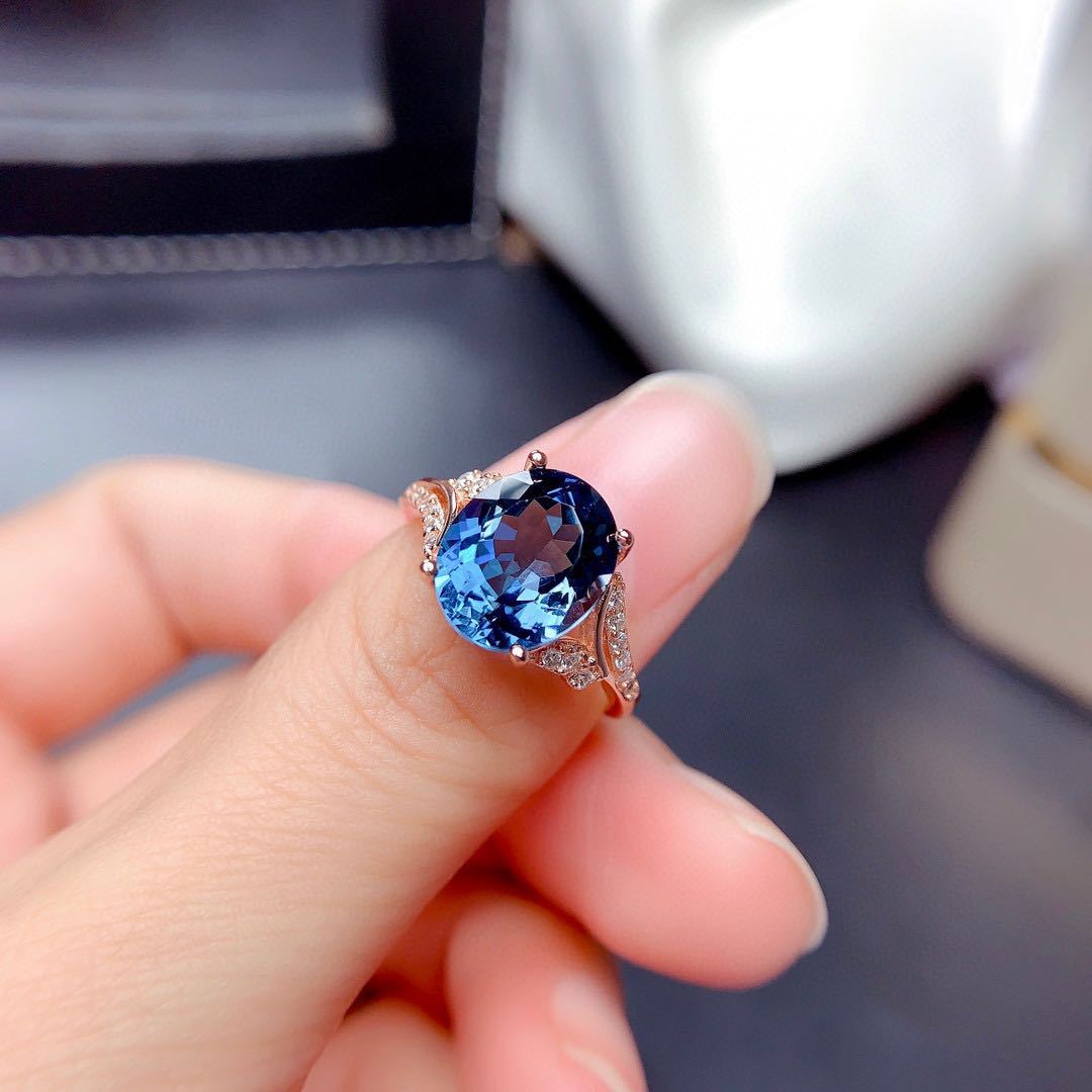 Blue gemstone ring held by a hand with a blurred background