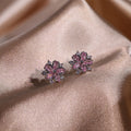 Pink flower-shaped earrings on a soft pink fabric background