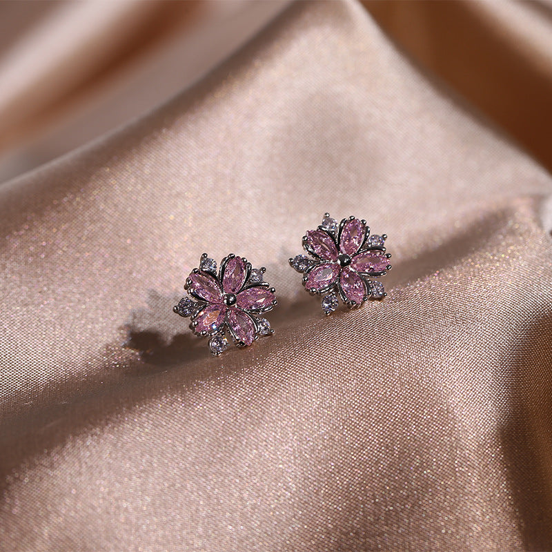 Pink flower-shaped earrings on a soft pink fabric background