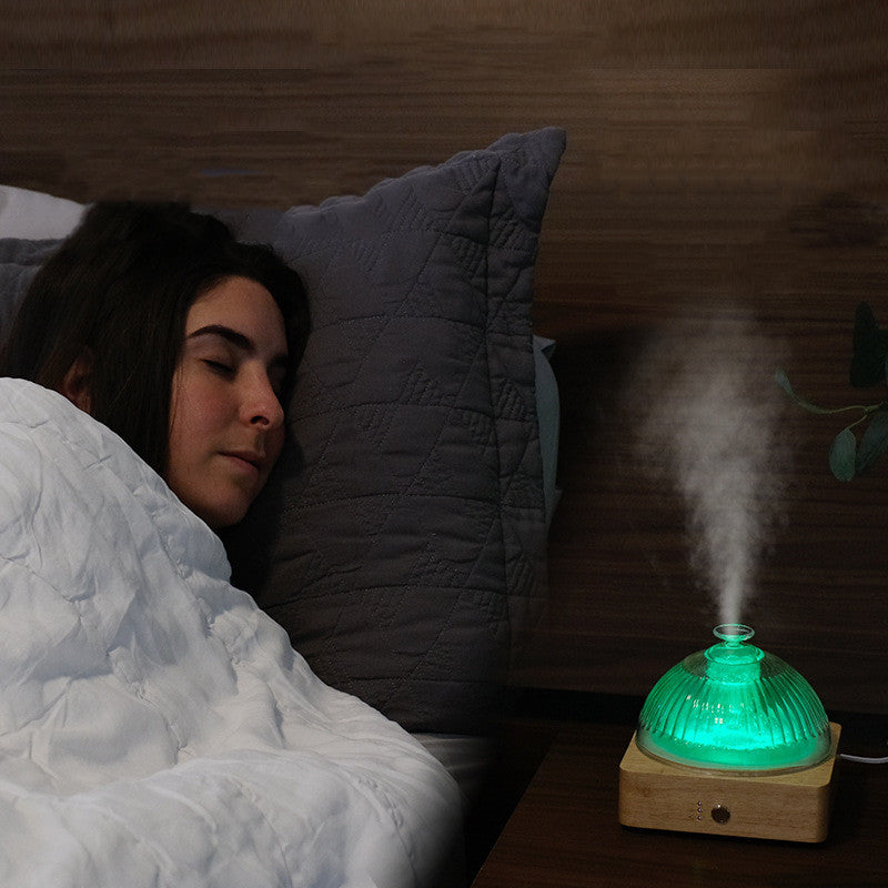 Person lying in bed with a humidifier emitting steam on a wooden nightstand.