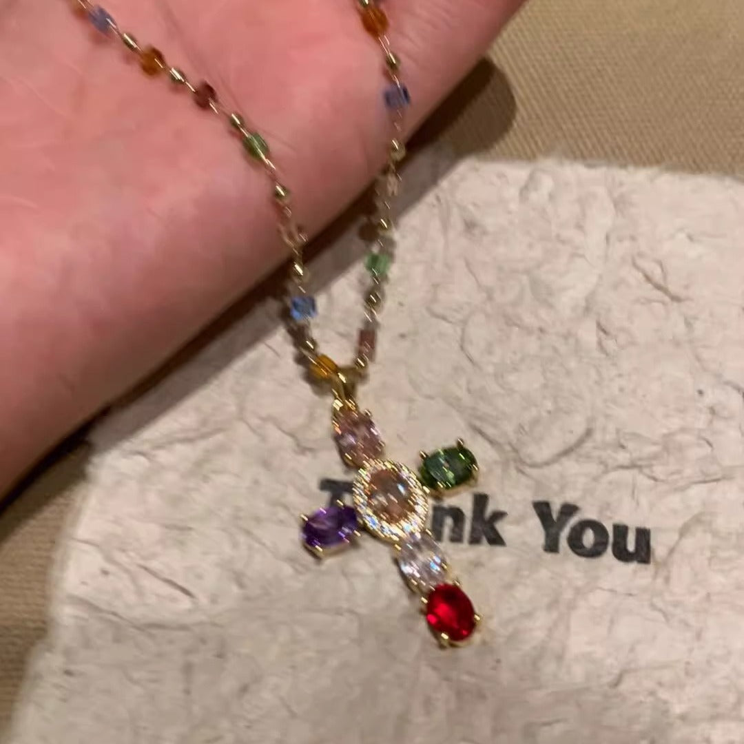 Necklace with a cross pendant featuring colorful gemstones on a textured surface.