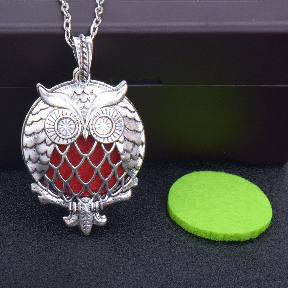 Silver owl pendant with red center on a dark surface with a green circular object.